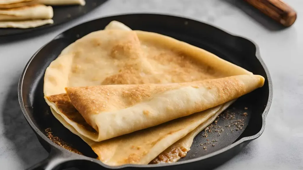 A golden brown crepe on a non-stick pan, showing the perfect thin and tender texture with crispy edges.